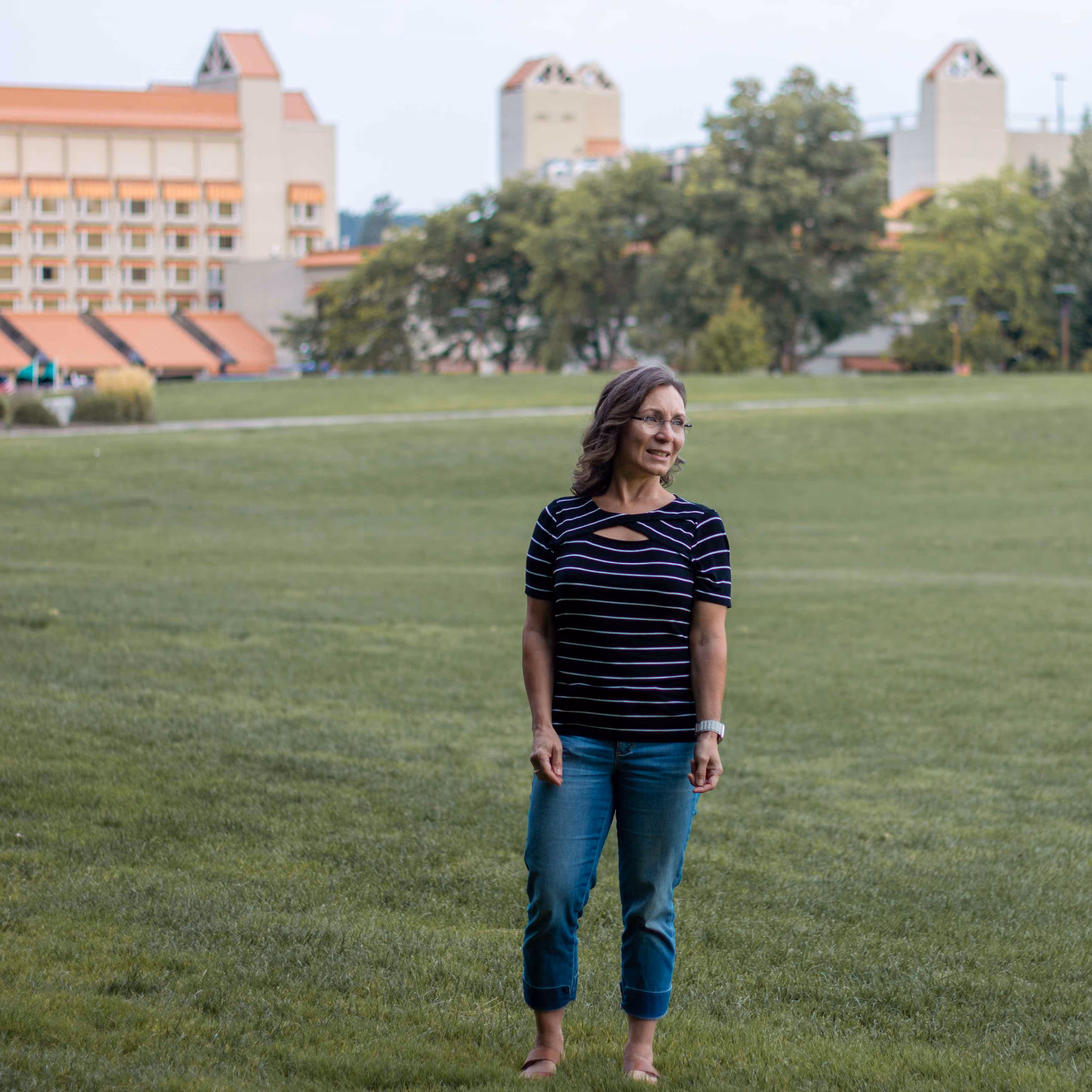 Woman wearing standing on green grass with buildings and trees in the background by Inlumina Creative.