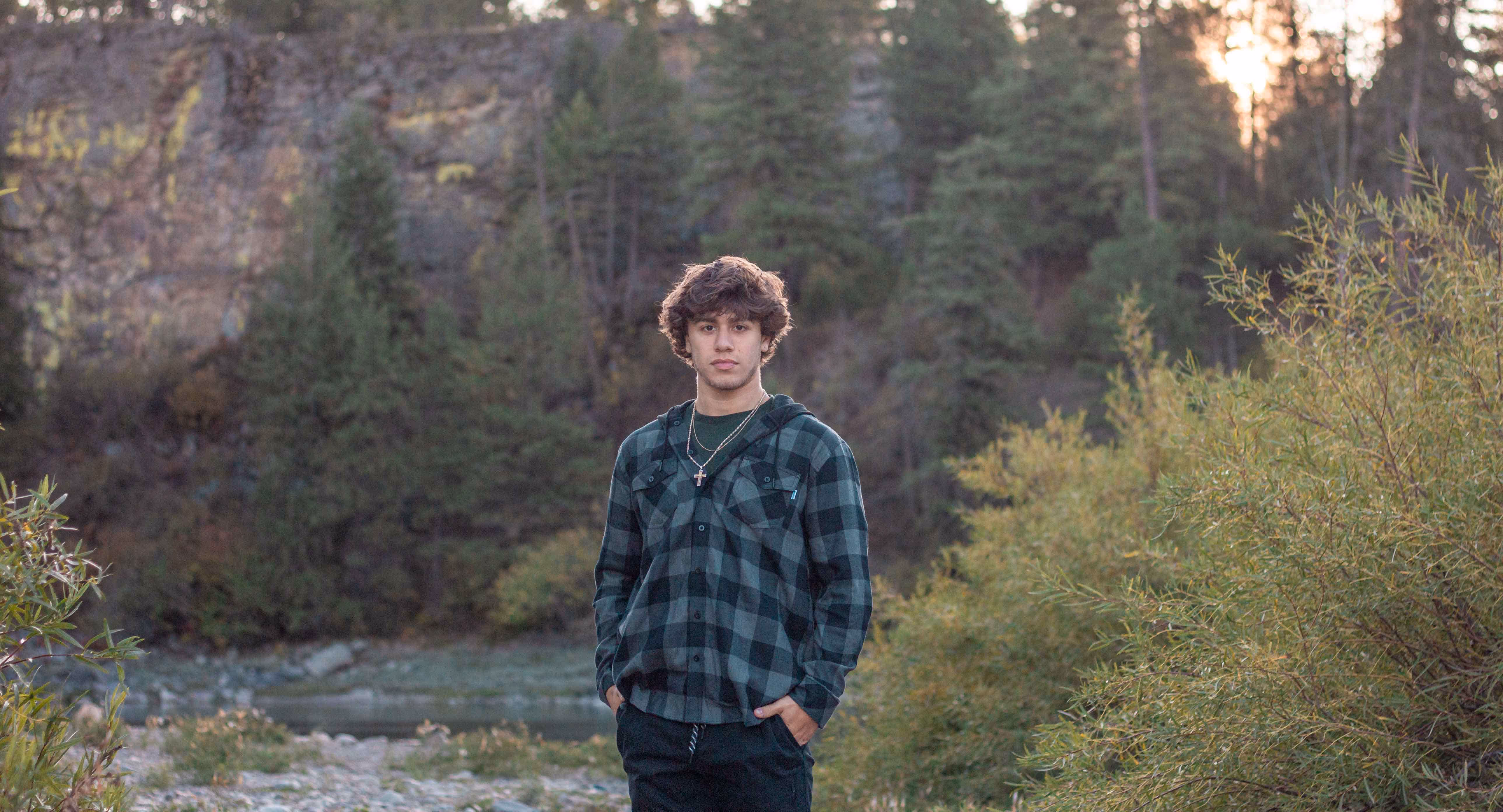 Young man standing outdoors front of river at dusk.