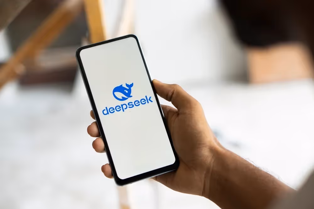 Hand holding smartphone displaying DeepSeek logo in blue on white screen