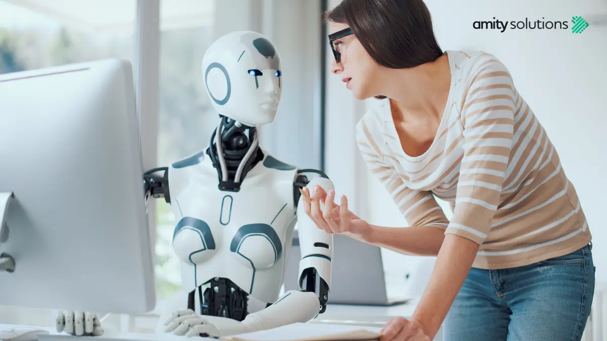 A humanoid AI robot and a woman collaborating at a computer in a modern office, illustrating how AI can work alongside humans to improve work-life balance.