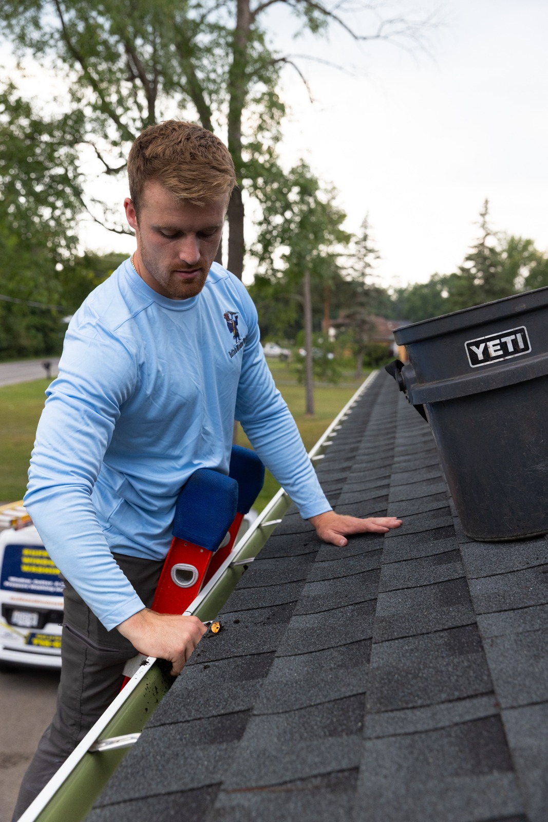 Technician cleaning gutter with bucket in front of him