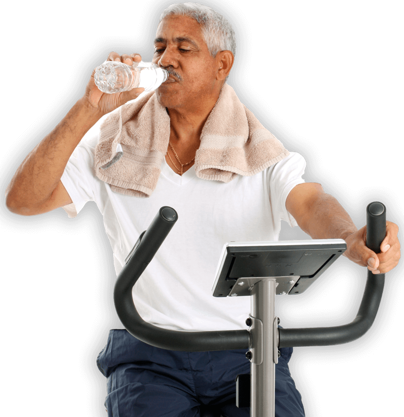 Older man on an exercise bike while drinking.