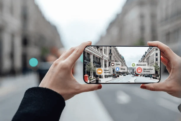 Two hands holding up a mobile phone at the street. The image of the street on the mobile phone is overlaid with tags like 
