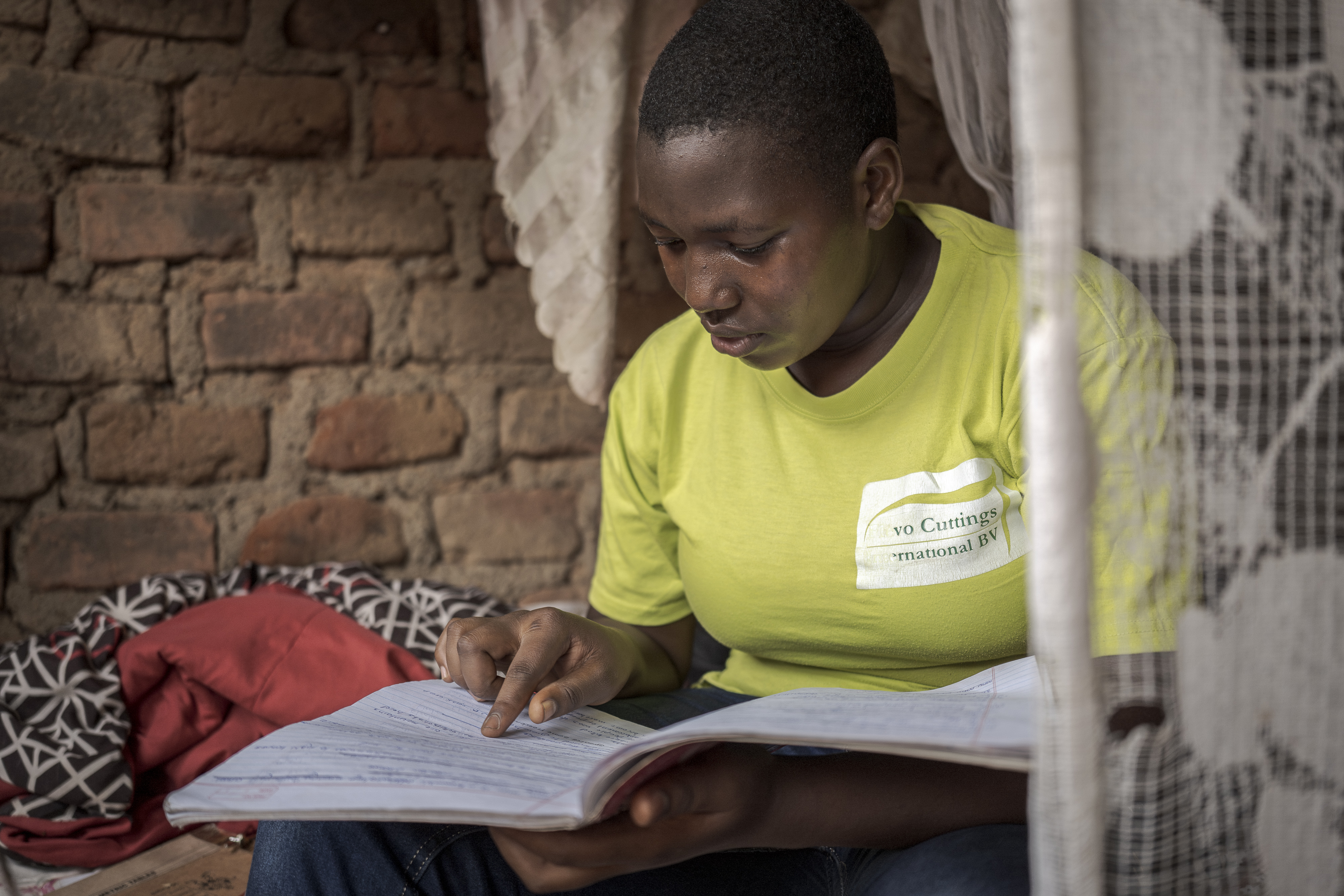 A girl with short hair wearing a yellow t-shirt studies the open notebook in her lap.