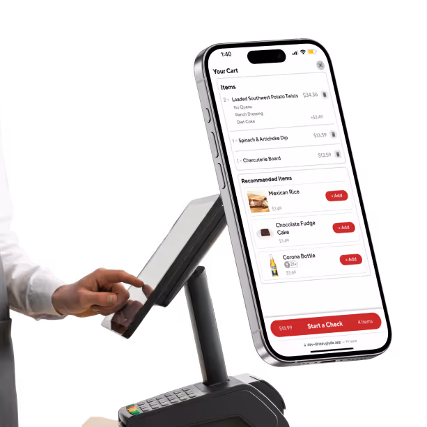 Person using touchscreen point-of-sale system next to a floating smartphone screen showing a shopping cart with food items and checkout options.