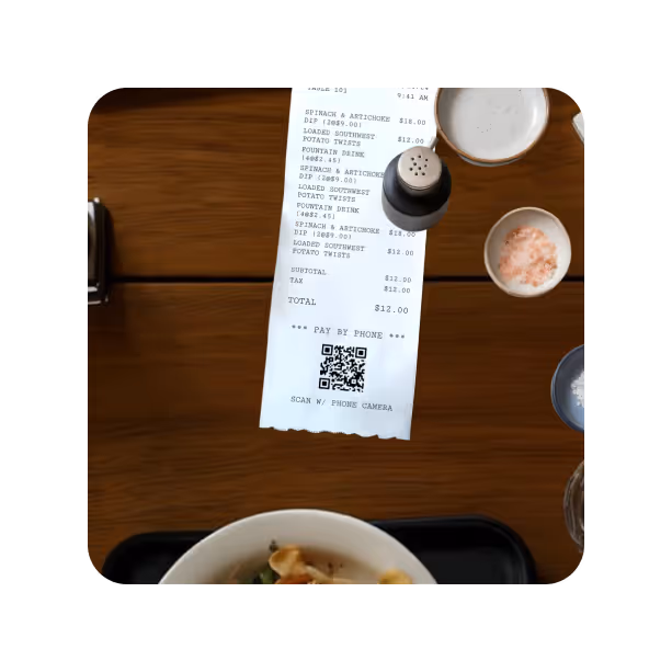 A restaurant receipt with a QR code for pay by phone on a wooden table alongside a salt shaker, bowl of pink salt, and a dish at the bottom.