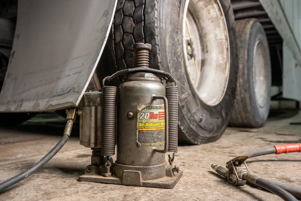 Bottle jack: Pittsburgh 20-ton air/hydraulic unit lifts semi-trailer axle, hose and coupler poised on shop floor.