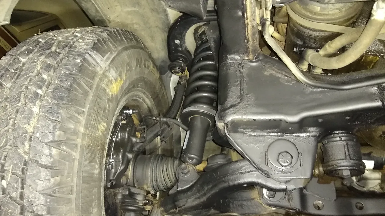 Suspension Repair close-up of truck front wheel, coilover and steering linkages, tire marked “RANG”.