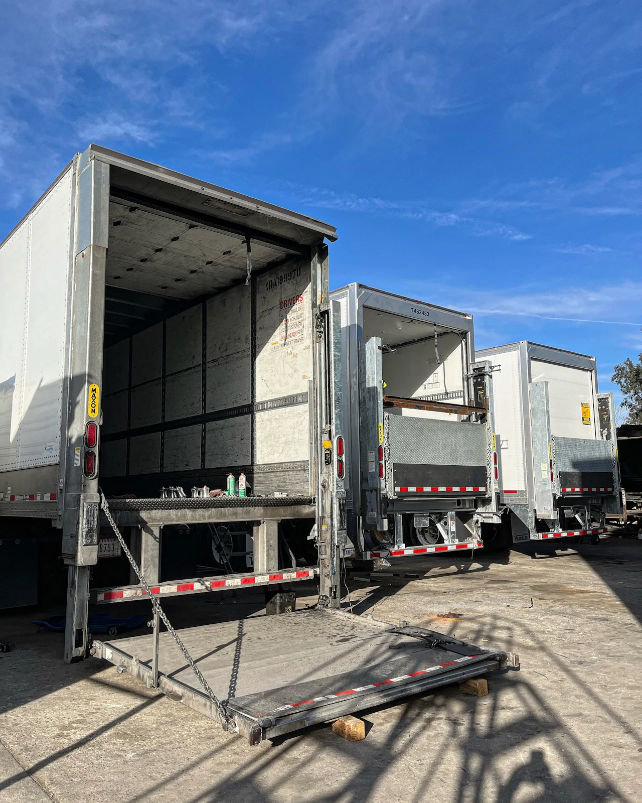 Hydraulic lift gate repair on multiple box trucks with rear lift platforms lowered for inspection, maintenance, and hydraulic system service.