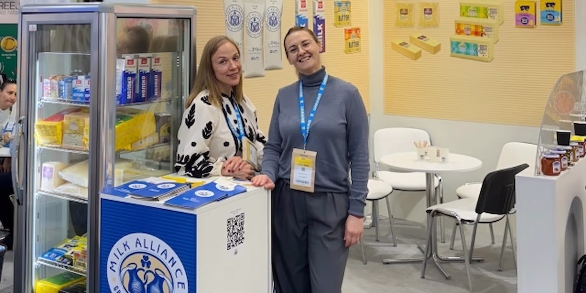 The blue-and-yellow product shelf with two Milk Alliance representatives at the SIAL Paris exhibition, highlighting Ukrainian food brands