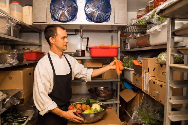 Man stocking a walk-in refrigerator, in a restaurant, with carrots. Restaurant equipment.