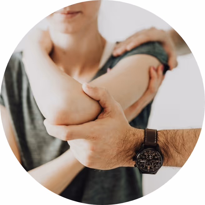 Person in einem grauen Shirt hält und streckt den gebeugten Ellbogen einer anderen Person vor einem unscharfen Hintergrund.