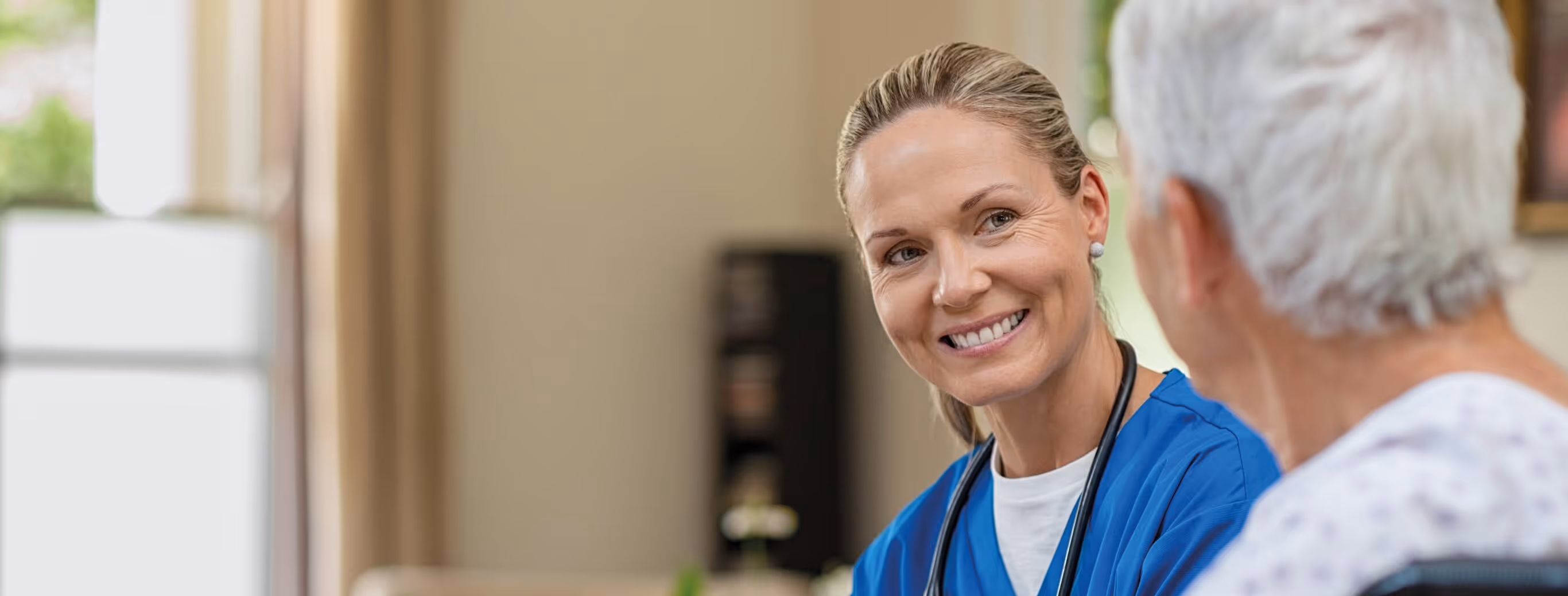 Ärztin in einer blauen Bluse spricht mit einem älteren Patienten im Krankenhaus.