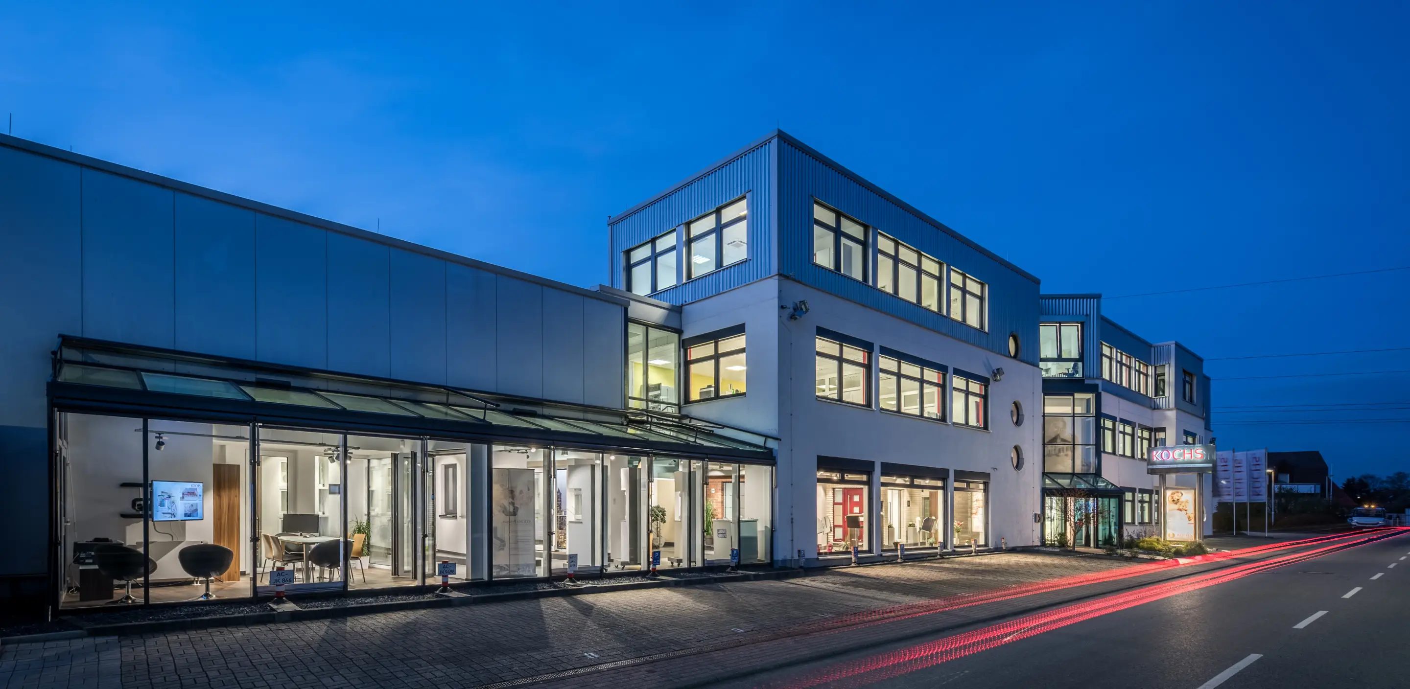 Modernes Ausstellungsgebäude mit großen Fenstern und beleuchtetem Innenraum bei Abenddämmerung