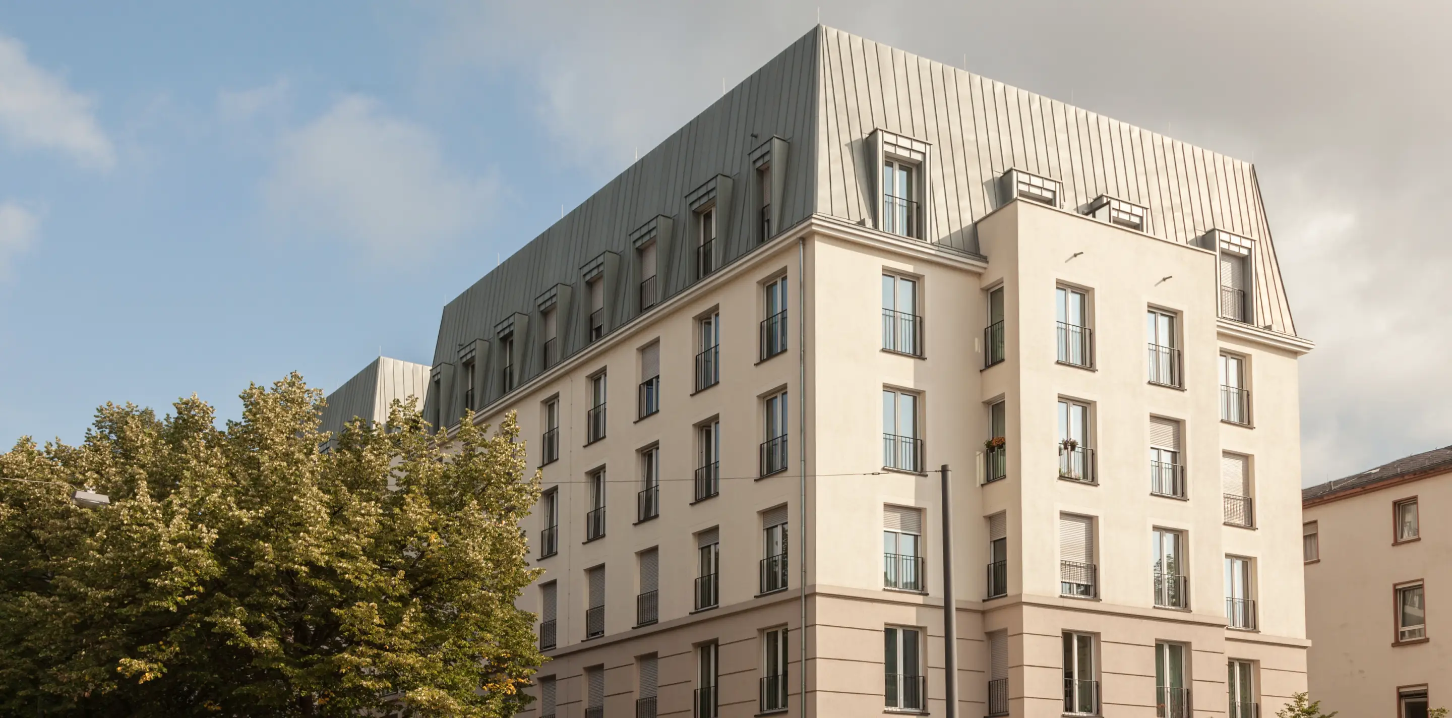Modernes Wohngebäude mit cremefarbener Fassade und grauem Dach bei bewölktem Himmel.