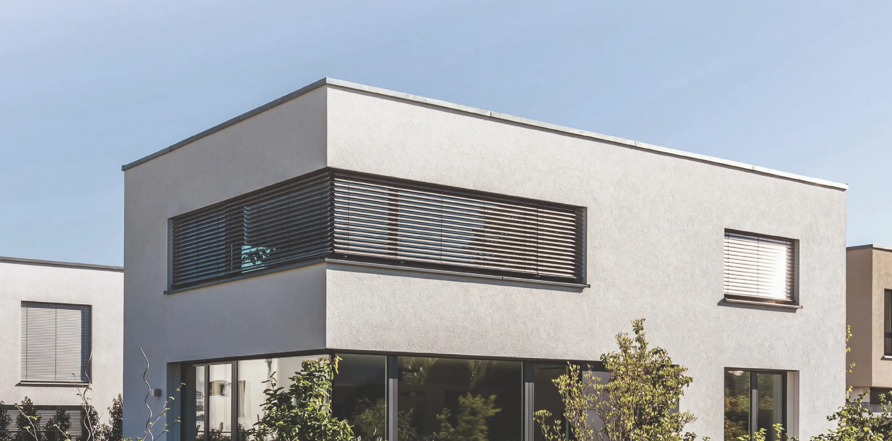 Modernes zweistöckiges Haus mit großen Fenstern und Jalousien unter klarem Himmel.