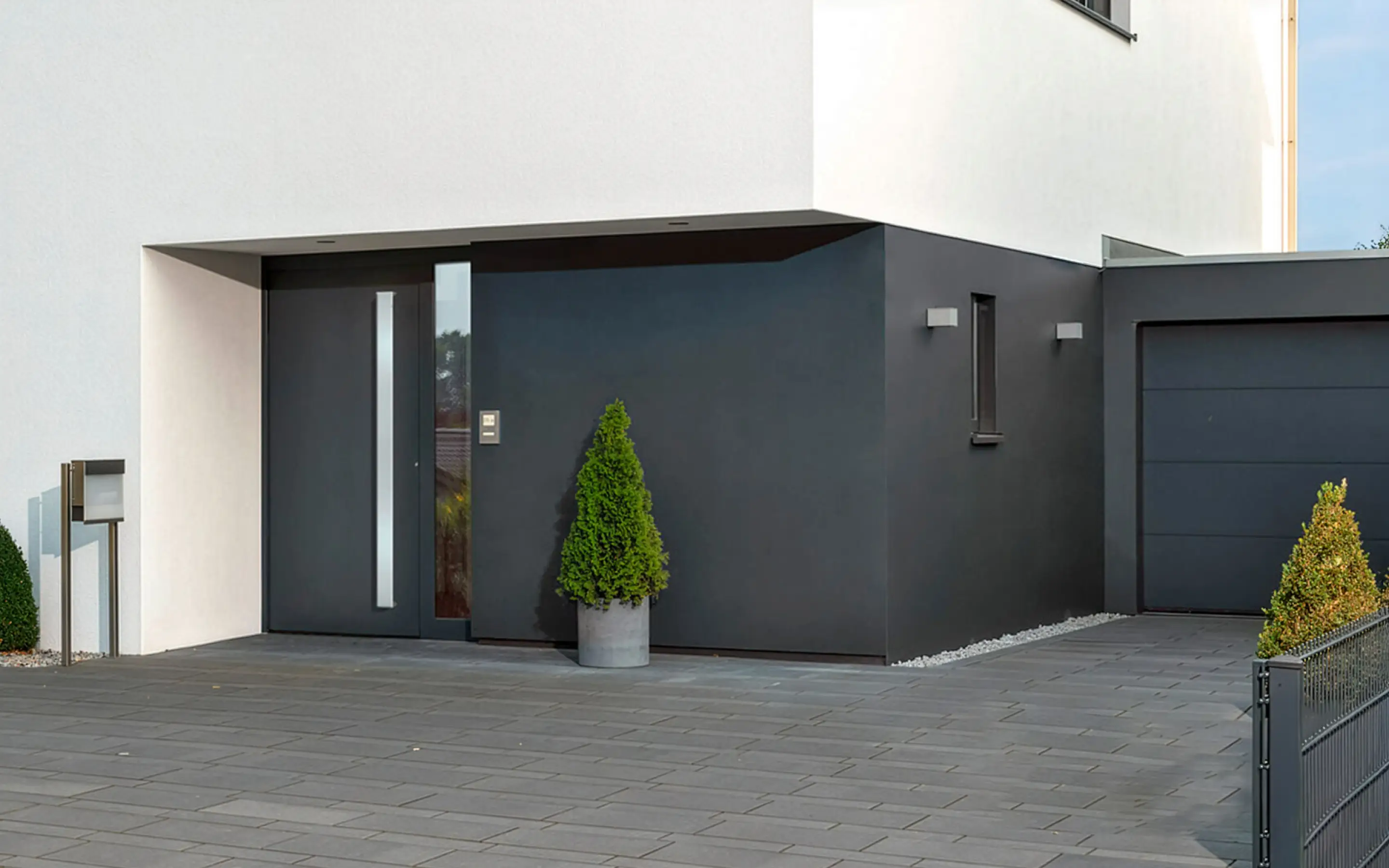 Moderne Hauseingangstür und Garage mit grauer Fassade und zwei grünen Zypressen im Topf.