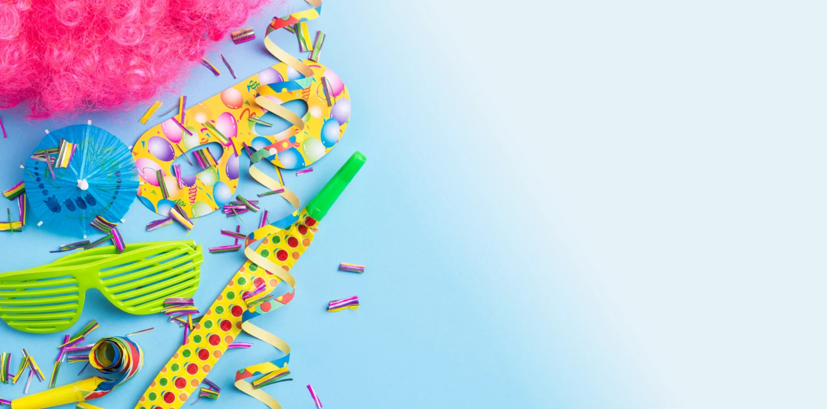 Bunte Partyartikel auf blauem Hintergrund, darunter grüne Sonnenbrille, blaues Cocktail-Schirmchen, gelbe Party-Tröte mit Punkten, Konfetti und bunte Luftschlangen.