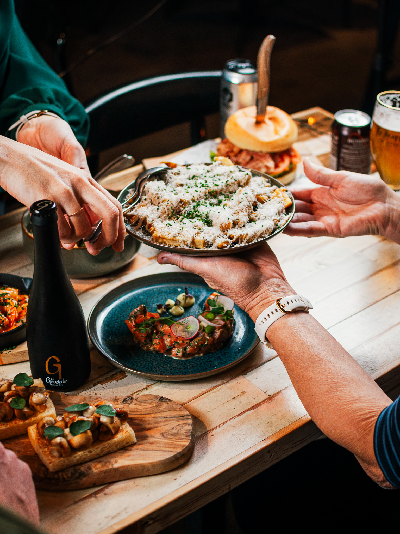 Handen schuiven schalen met bites en gerechten over een houten tafel met bier