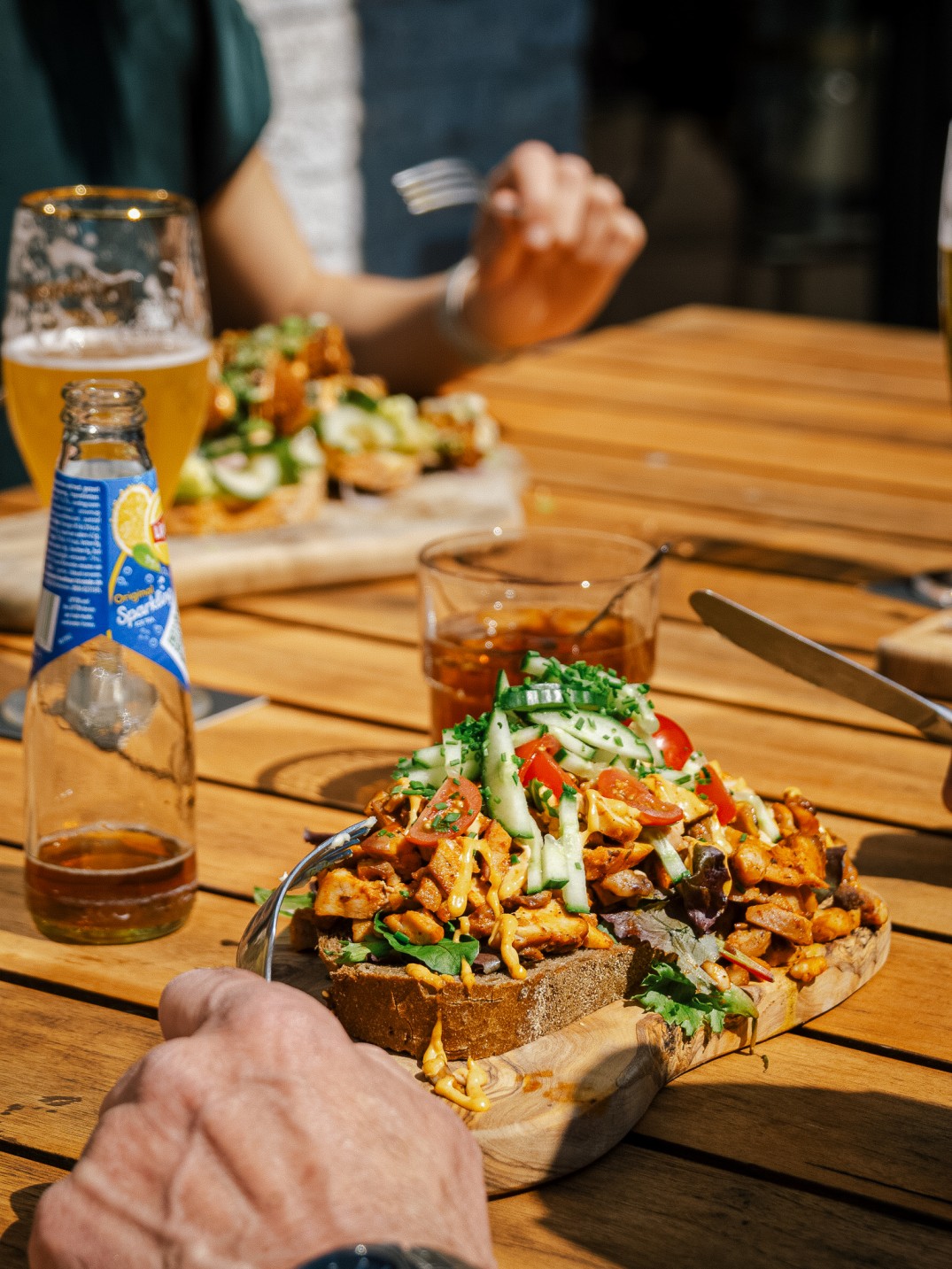 Kipgerecht met komkommer en tomaat op brood, met een glas bier op een terrastafel