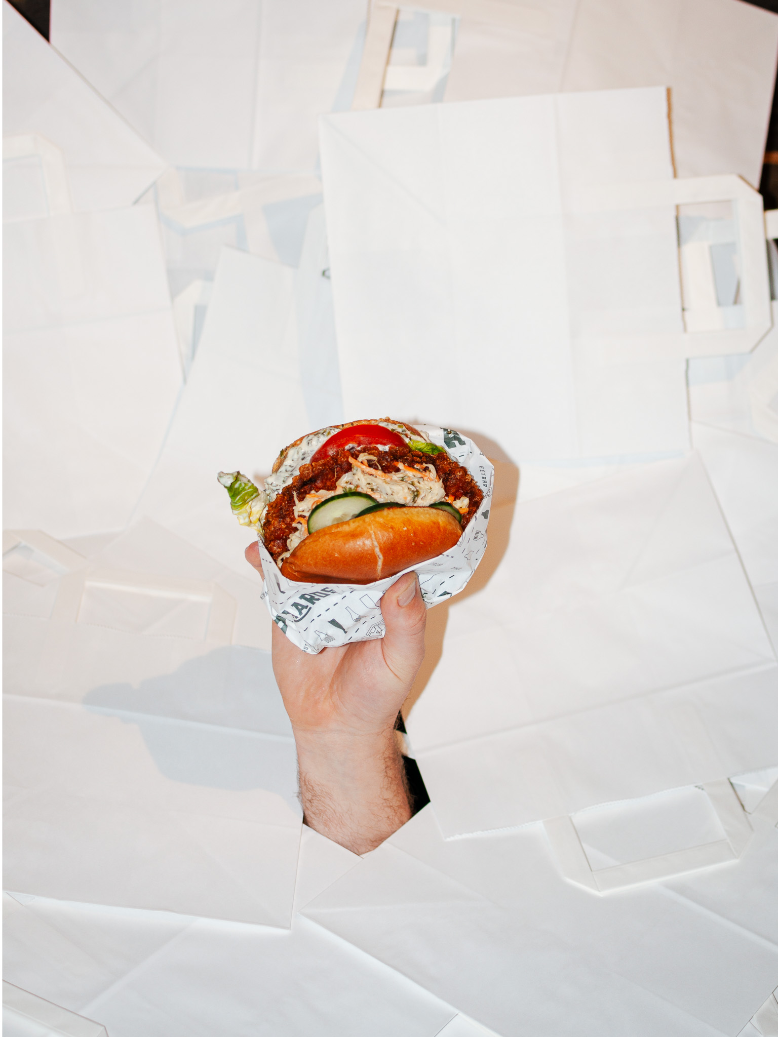 Hand houdt een broodje met burger tegen een witte achtergrond