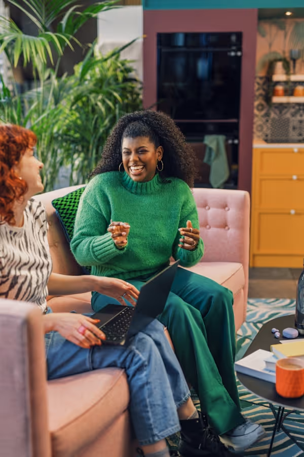 a person sitting on a couch with a laptop and a person holding a cup