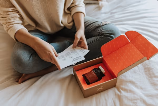 Woman sitting on bed while reading package materials included within the Nouri subscription box. 