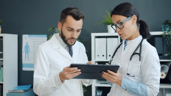 Medics in white gowns young man and woman are using tablet at work talking using gadget in office. Modern devices, people and technology concept.