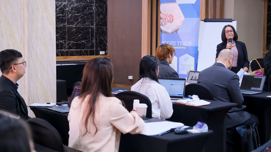 People attending a business seminar, listening to a speaker at the front of the room.