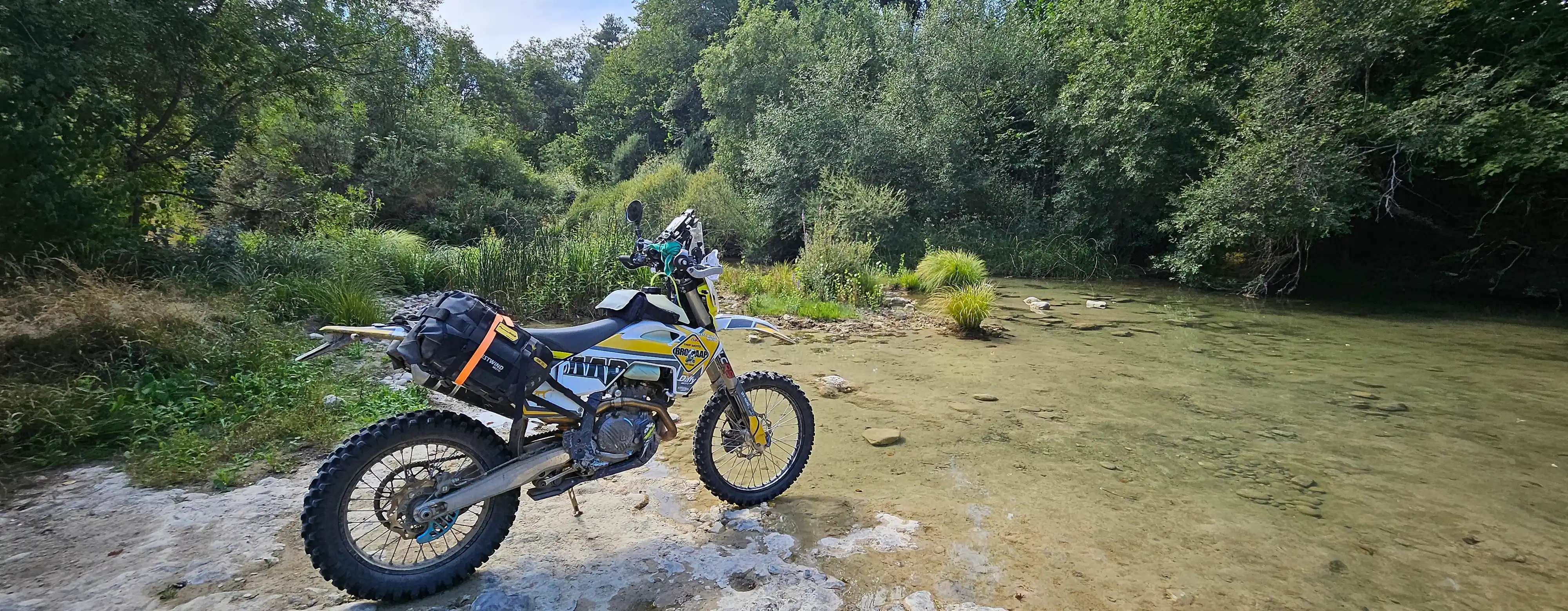 Moto trail chargée à l’arrêt au bord d’une rivière lors d’une randonnée off-road