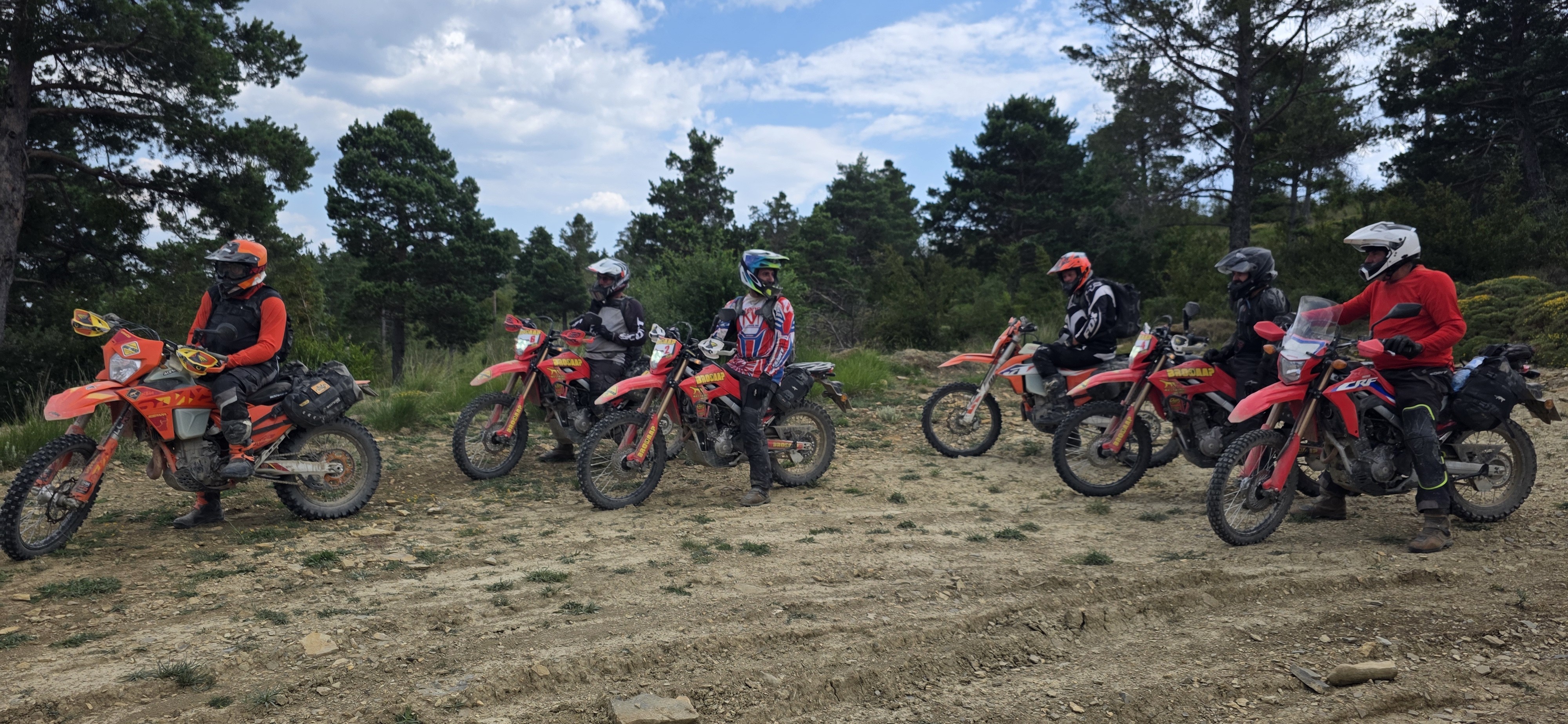 Groupe de six pilotes et leurs motos trail à l’arrêt lors d’une pause en clairière