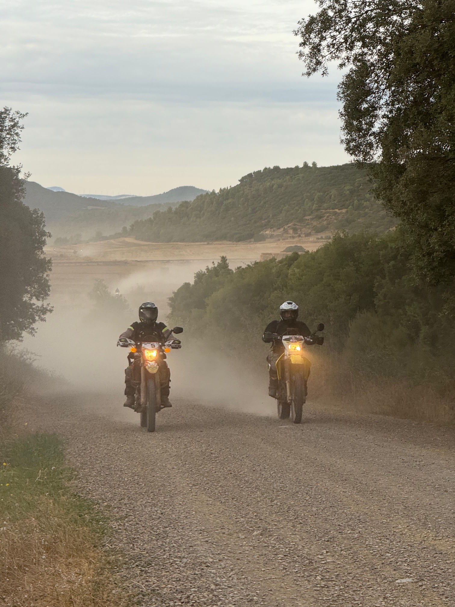 Deux motards trail roulant phares allumés sur une piste poussiéreuse
