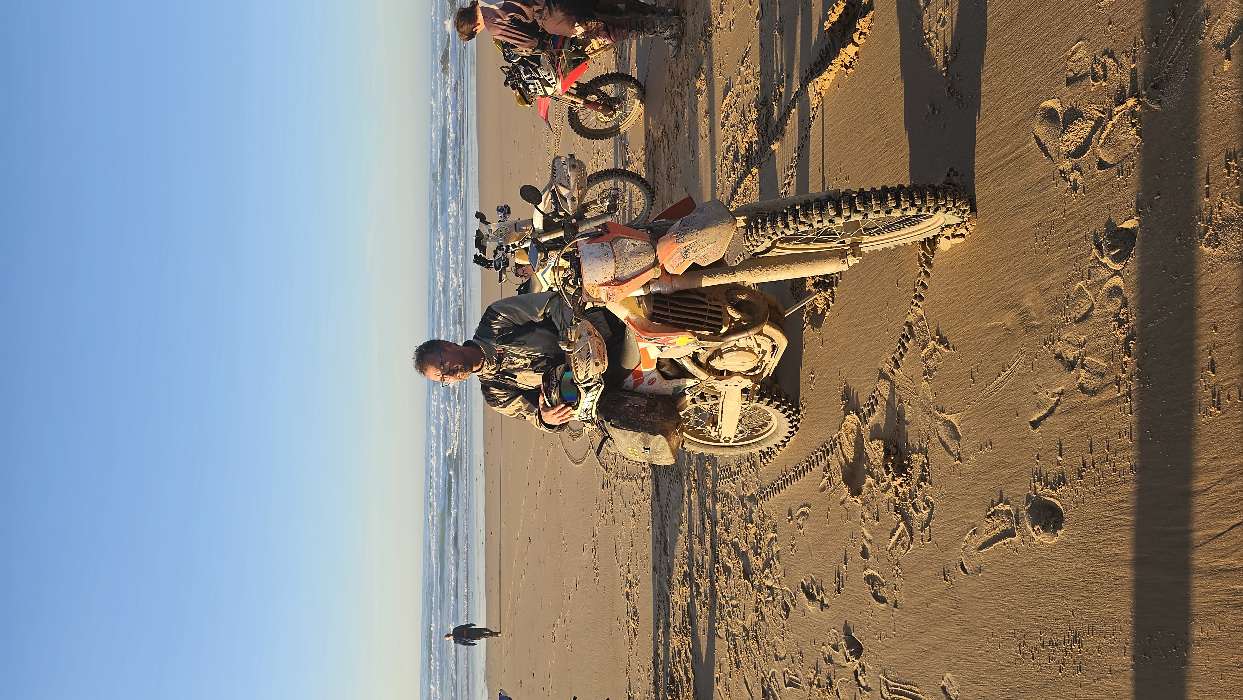 Motard sur sa moto d’enduro sur une plage de sable face à l’océan