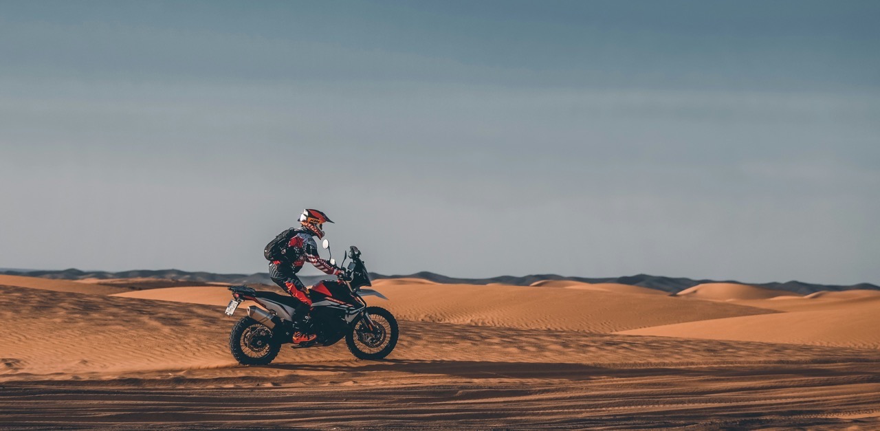 Pilote sur une moto trail roulant dans les dunes de sable du désert