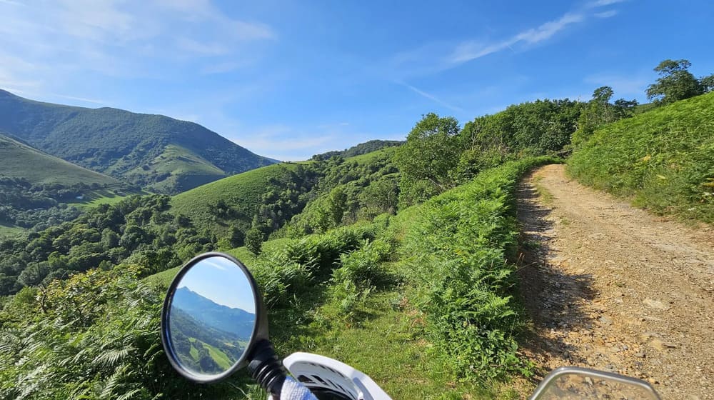 Piste de terre en balcon sur des collines verdoyantes vue depuis la moto