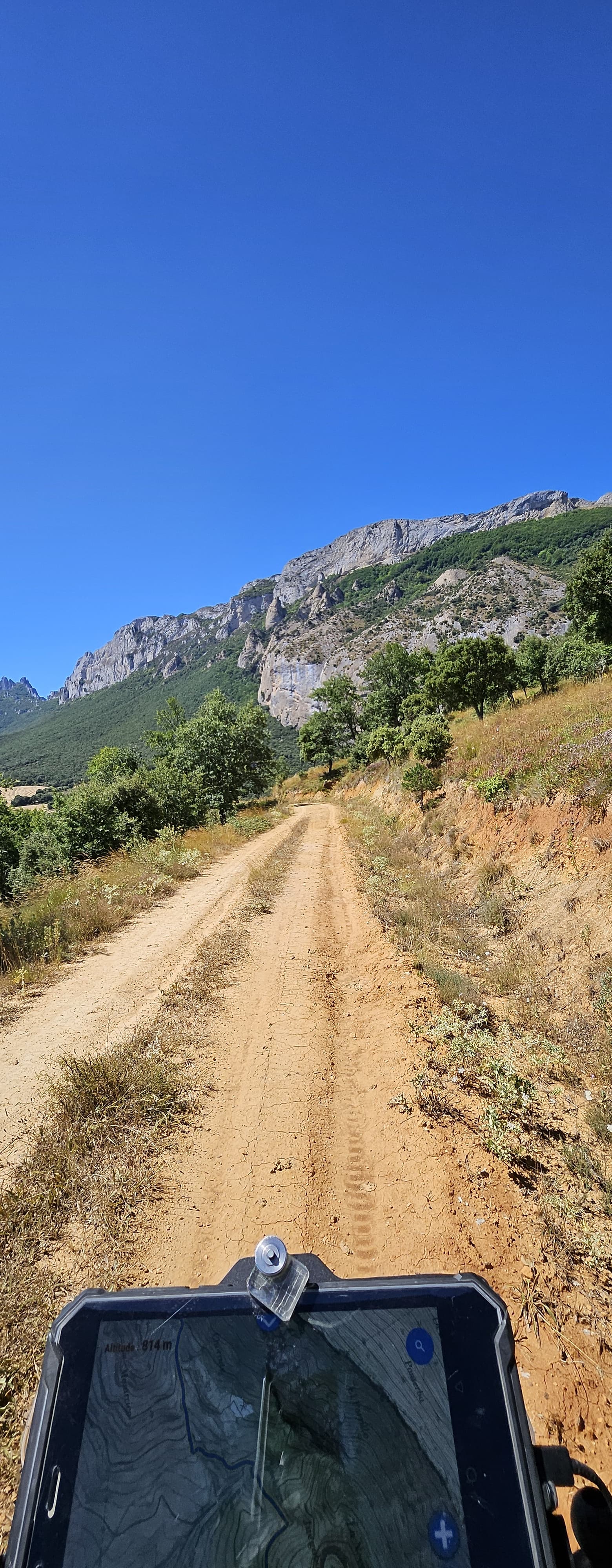 Piste de terre filant vers des falaises calcaires, vue depuis la moto