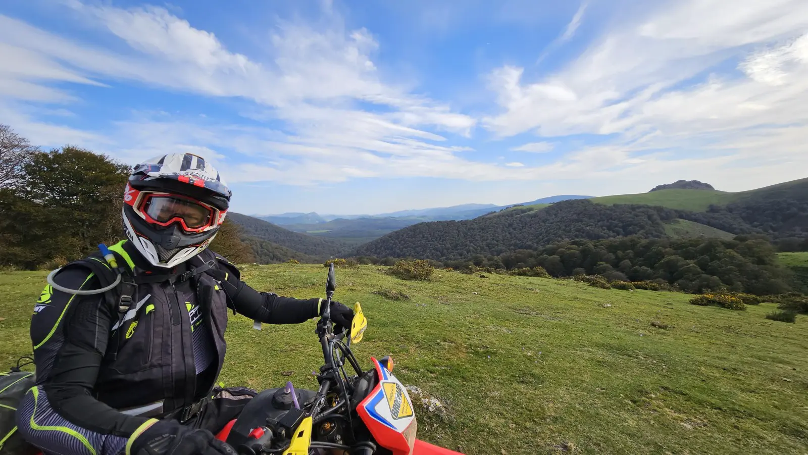 Motard casqué sur sa moto d’enduro face à des collines verdoyantes