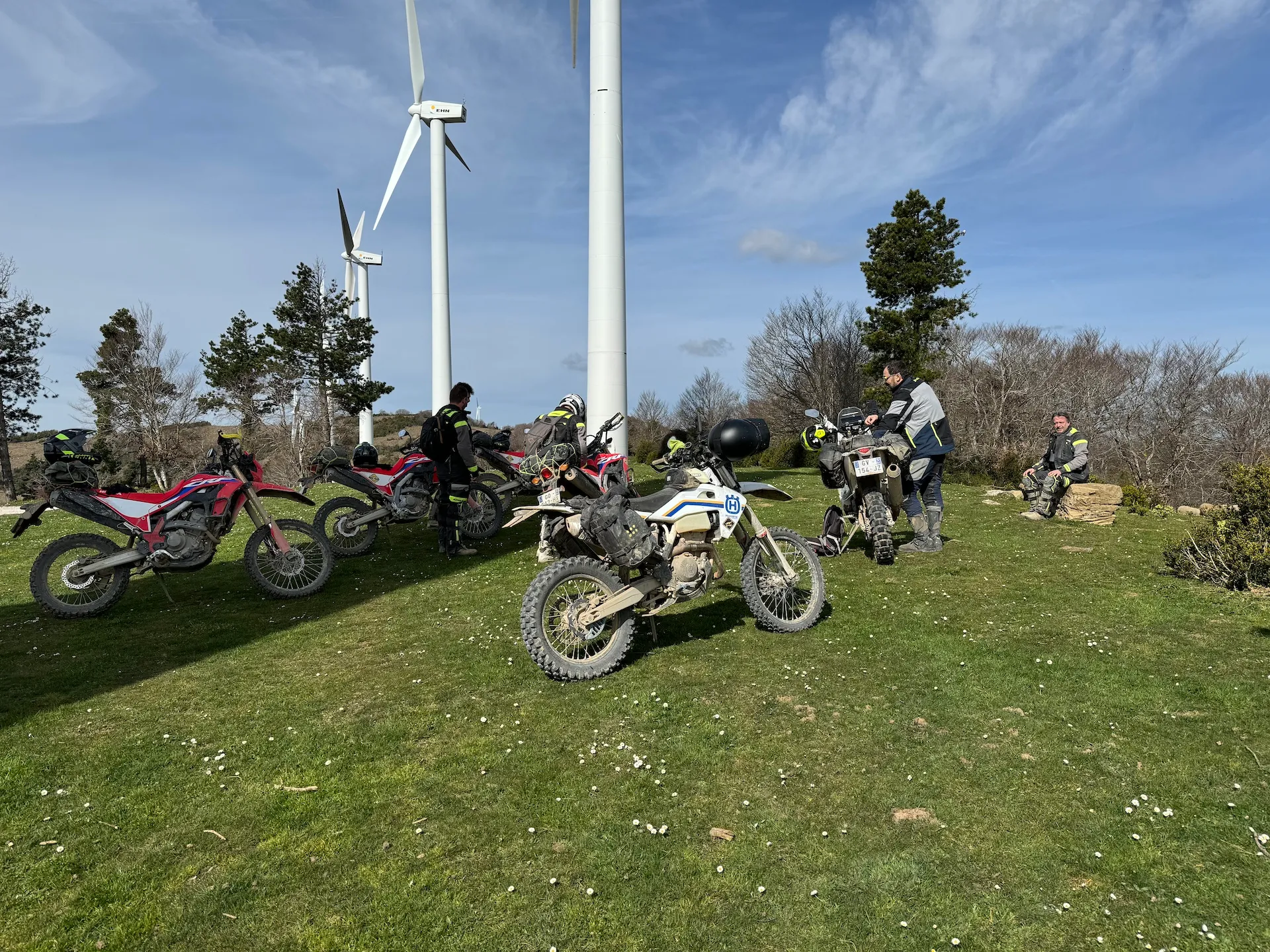 Motos trail garées sur l’herbe au pied d’éoliennes