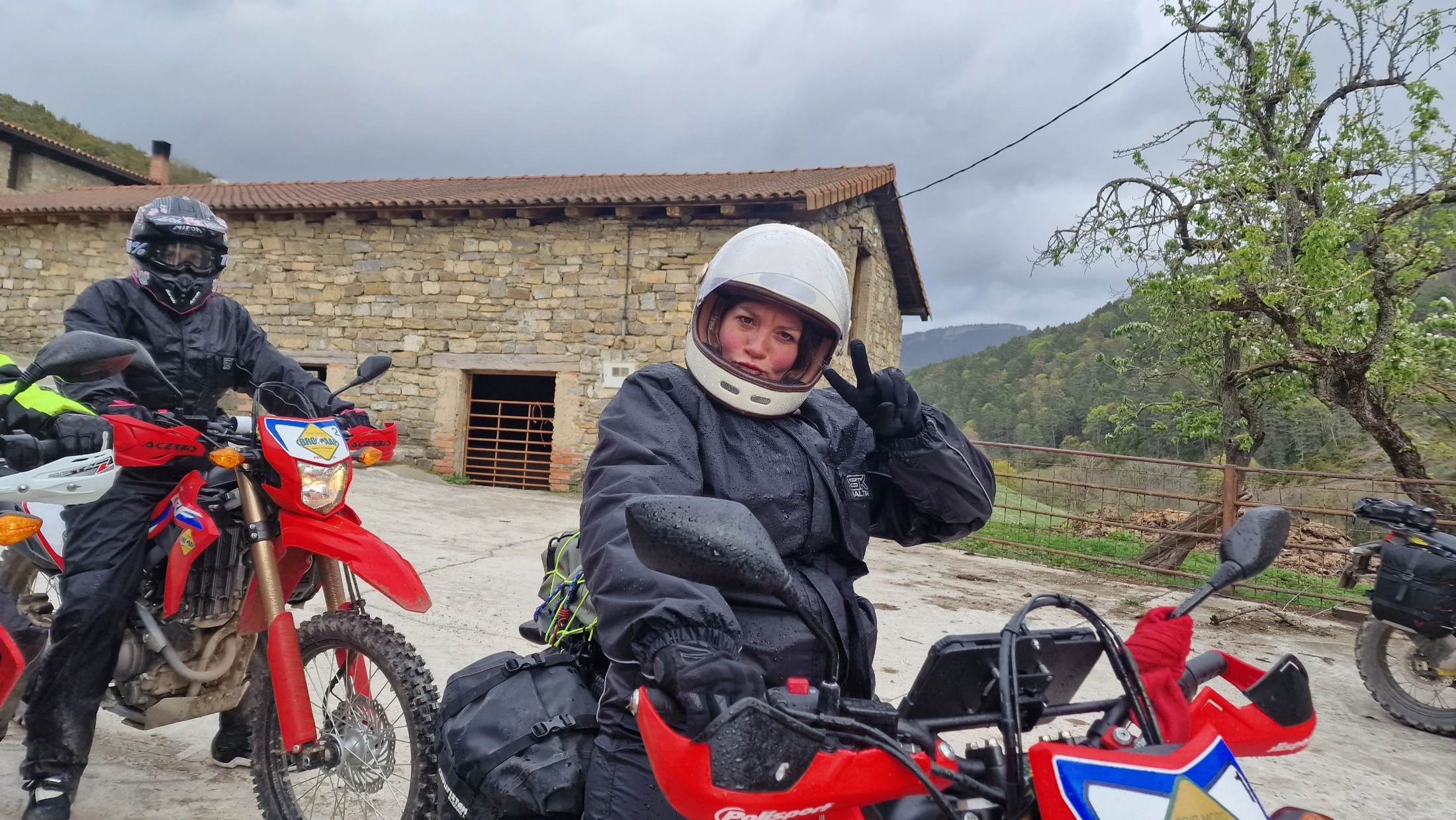 Motardes souriantes près de leurs motos d’enduro devant une ferme