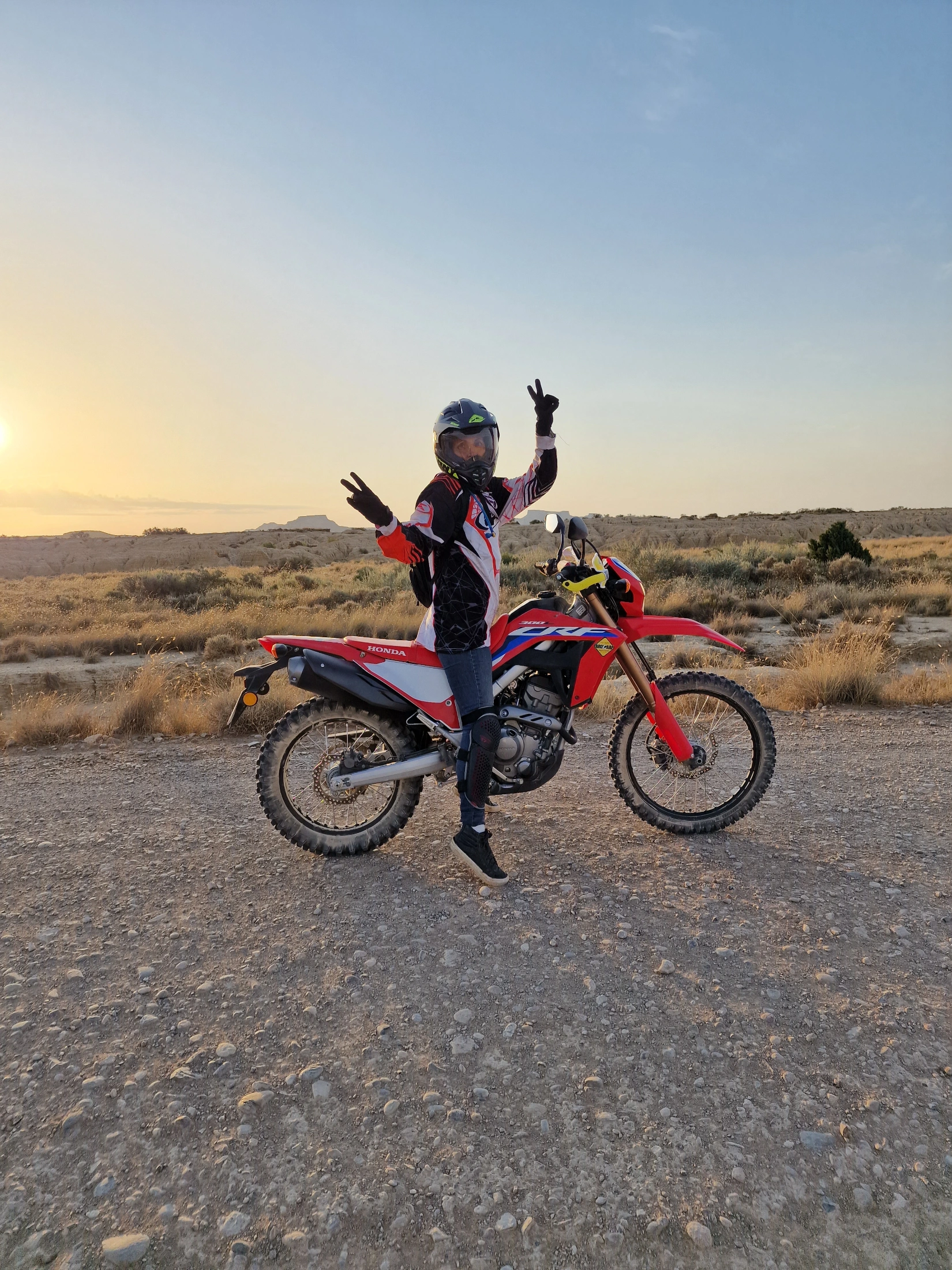 Motarde faisant le signe de la victoire près de sa moto au coucher du soleil