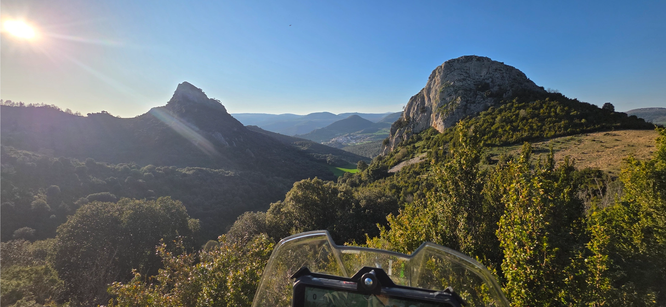 Pitons rocheux et collines boisées au soleil, vus depuis la moto
