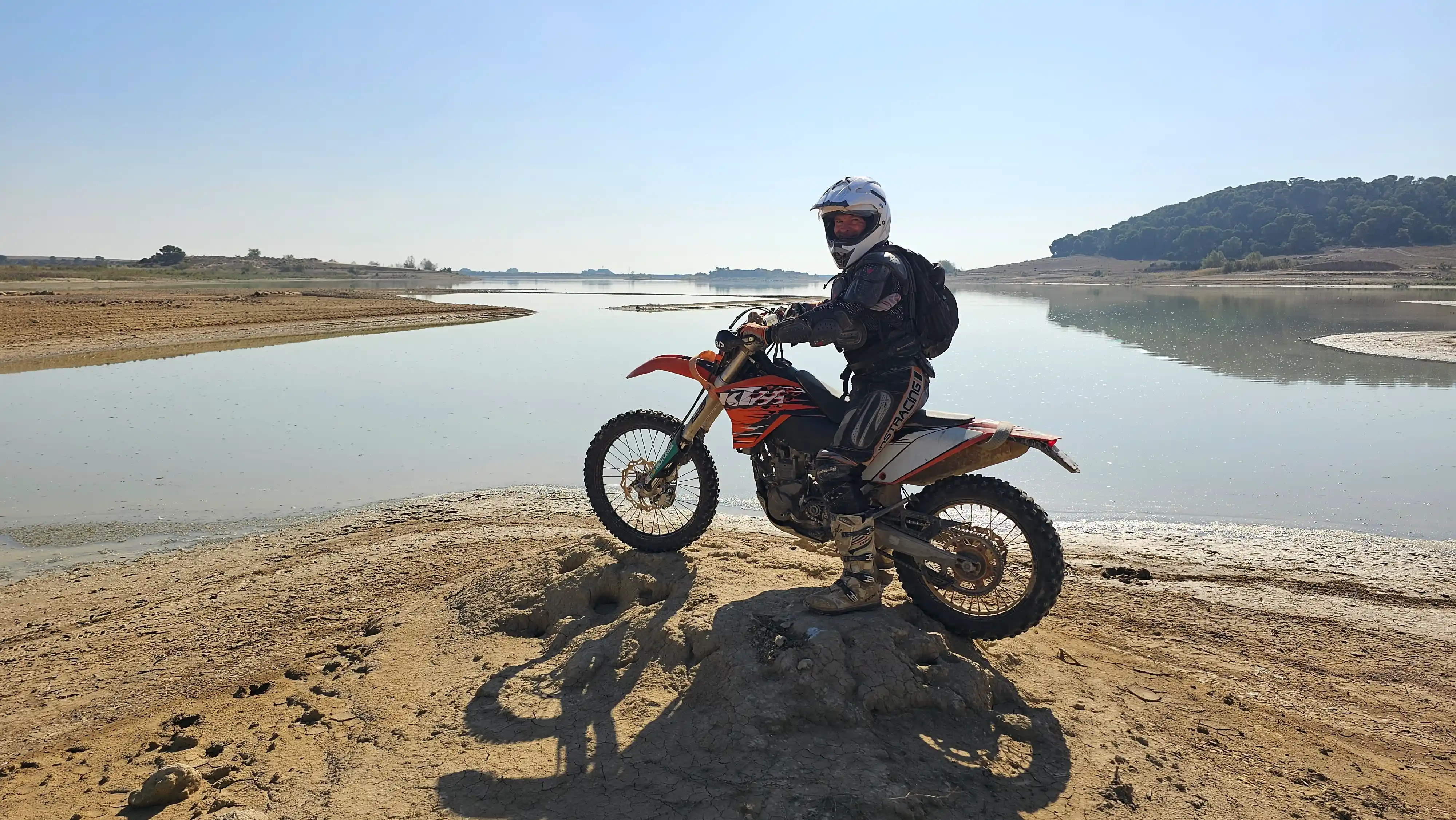 Motard d’enduro posant sur la rive d’un lac au soleil