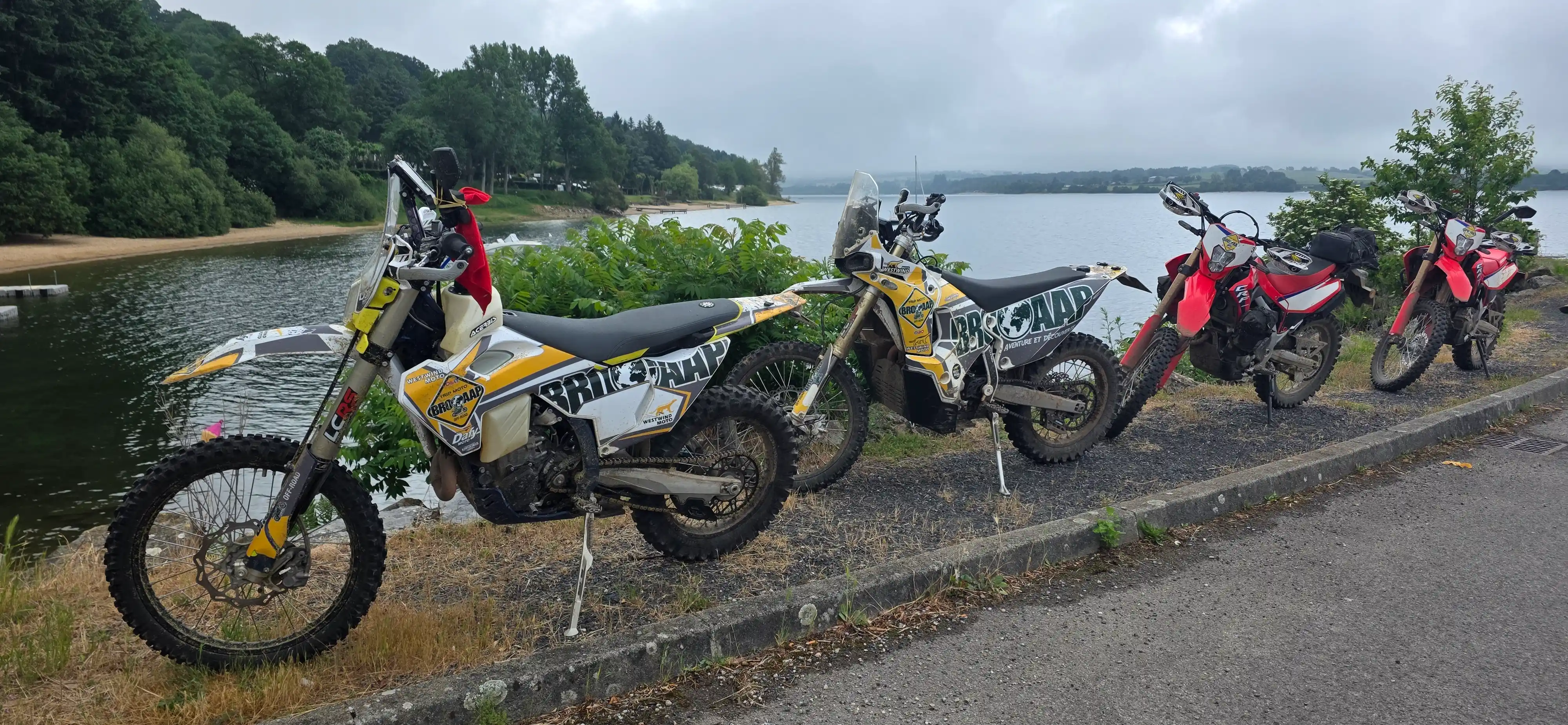 Motos trail garées au bord d’un lac entouré de forêts