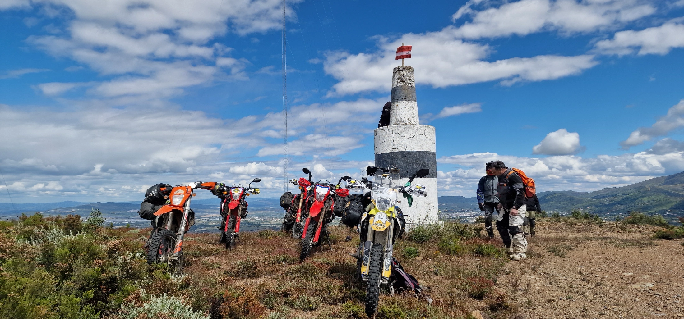 Motos d’enduro au pied d’une borne géodésique sur une colline