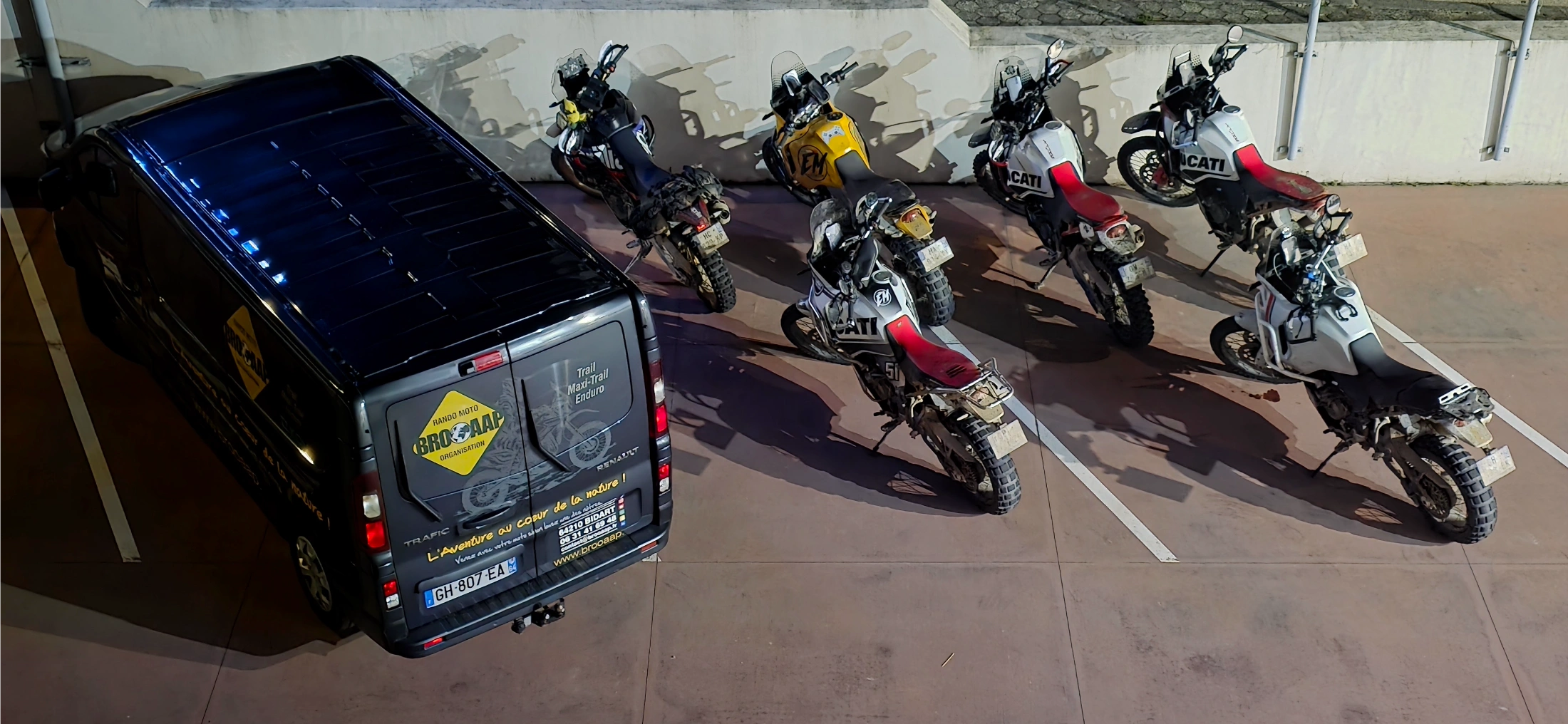 Motos trail et fourgon Brooaap garés sur un parking couvert