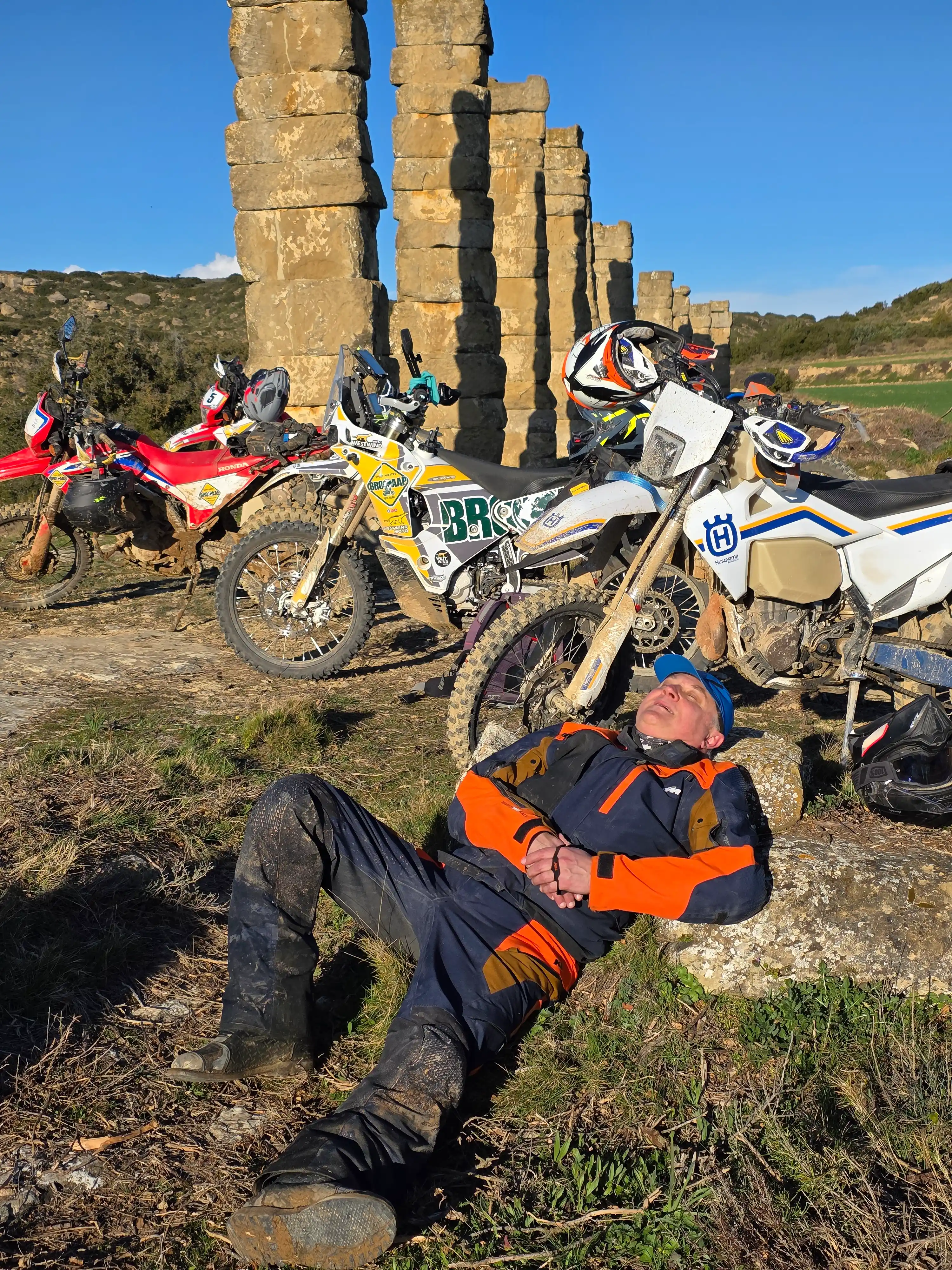 Motard allongé dans l’herbe devant des motos et des colonnes de pierre