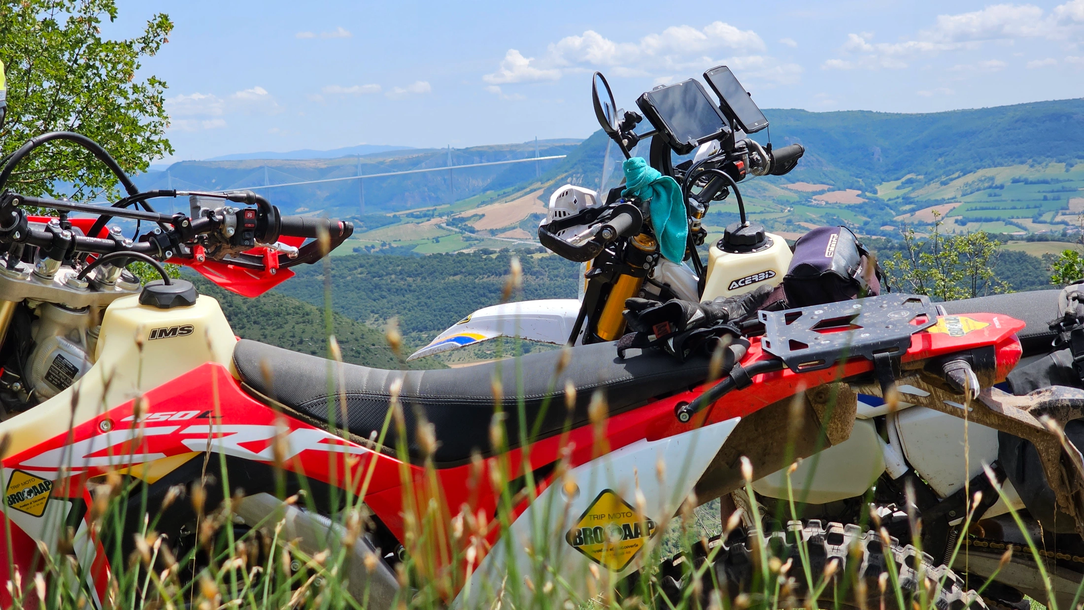 Motos d’enduro équipées de GPS garées face à une vallée de l’Aveyron