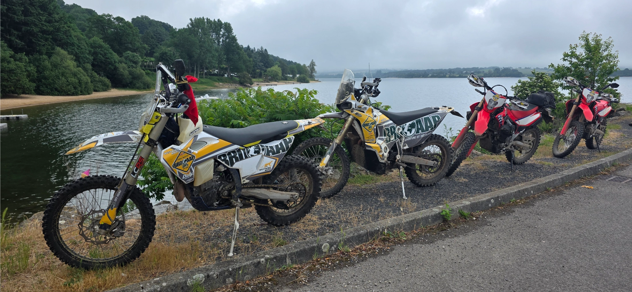 Motos trail garées au bord d’un lac entouré de forêts