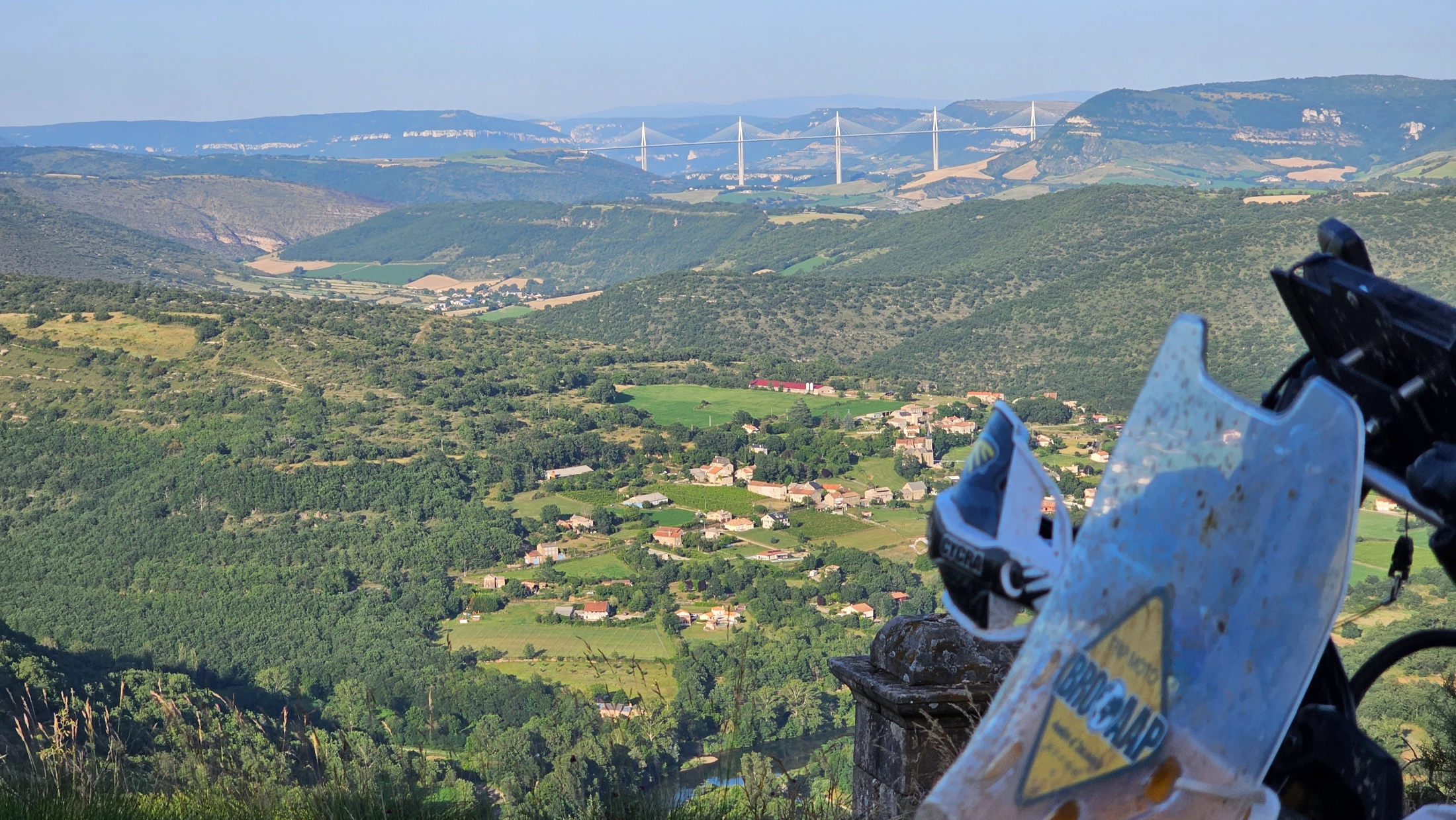 Vallée boisée et viaduc de Millau au loin, vue depuis une moto