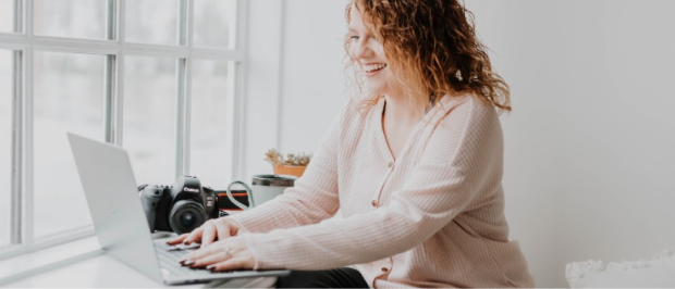 A woman sitting on a window sill using a laptop